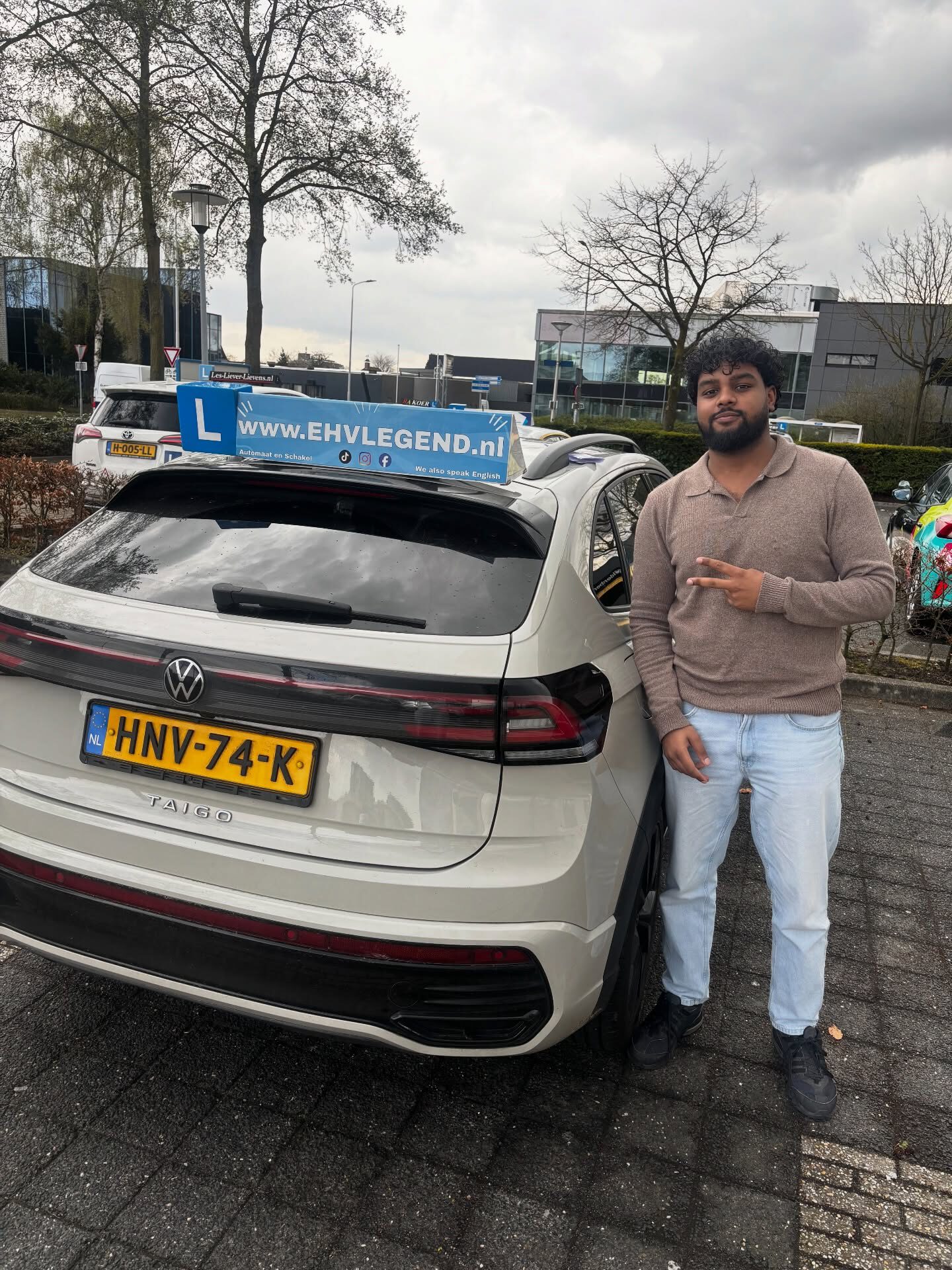 Geslaagde cursist van Rijschool EHVLegend poseert trots naast lesauto met kenteken HNV-74-K